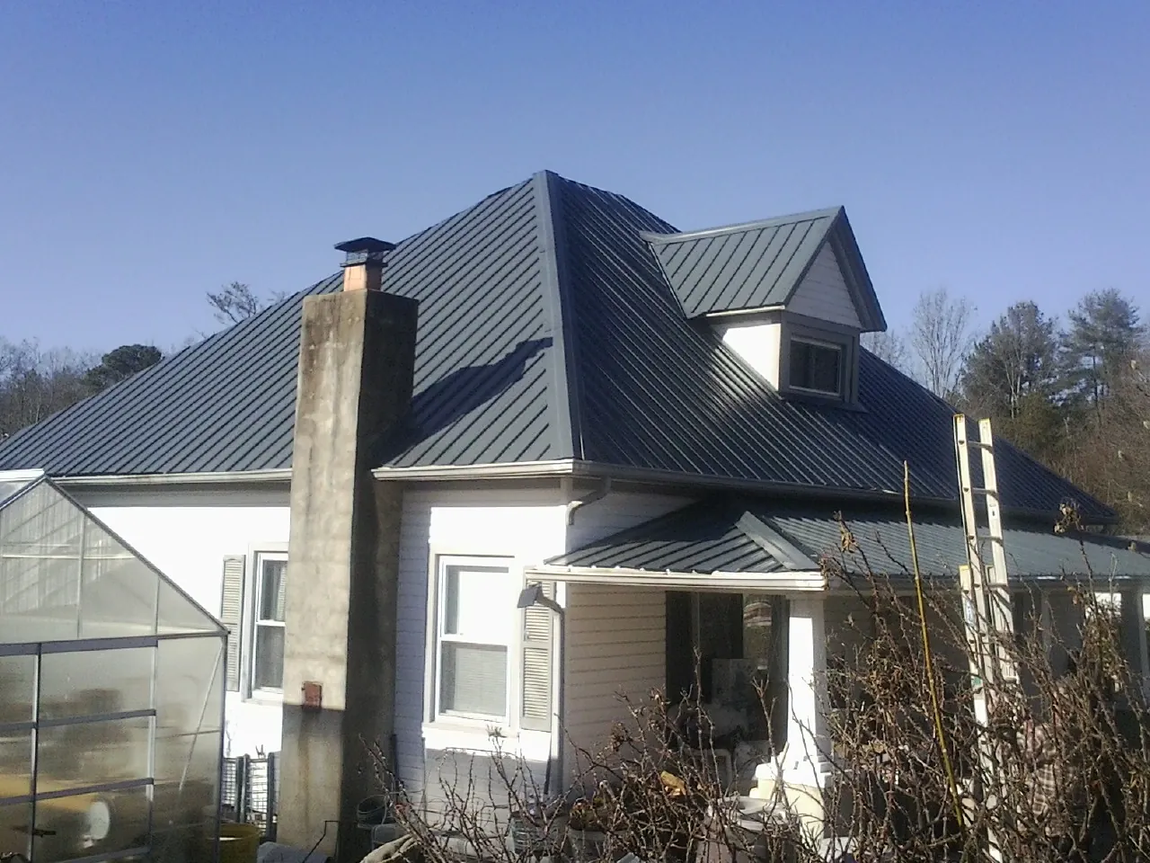 Dark blue standing seam metal roof on a white farmhouse with dormer — Slate & Tile Roof Repair by Roofing Brothers in Minoa
