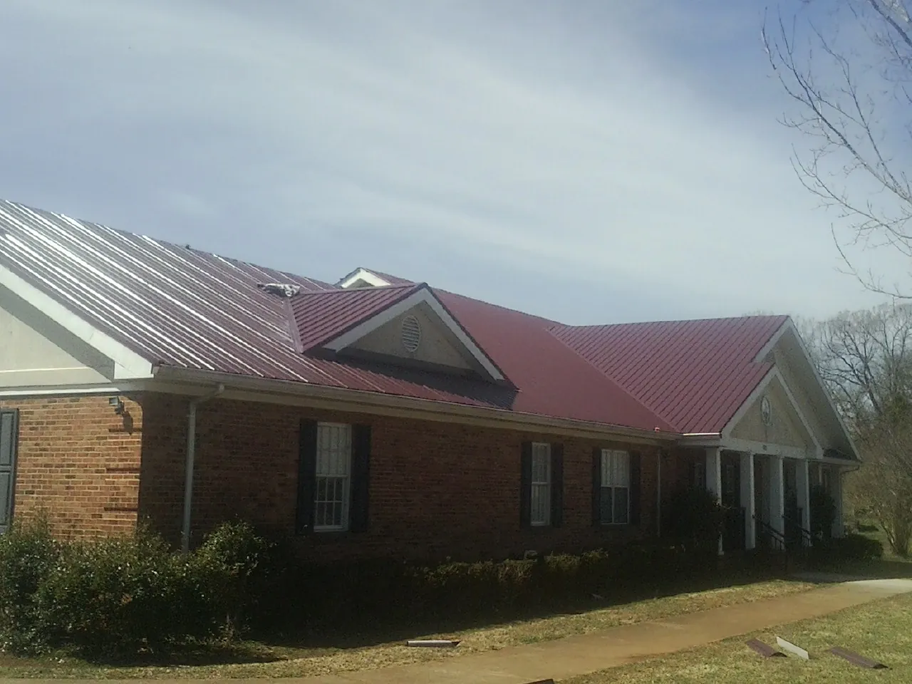 Red metal roof with gabled entries on a long brick building, from a Hail Damage Roof Repair job in Minoa