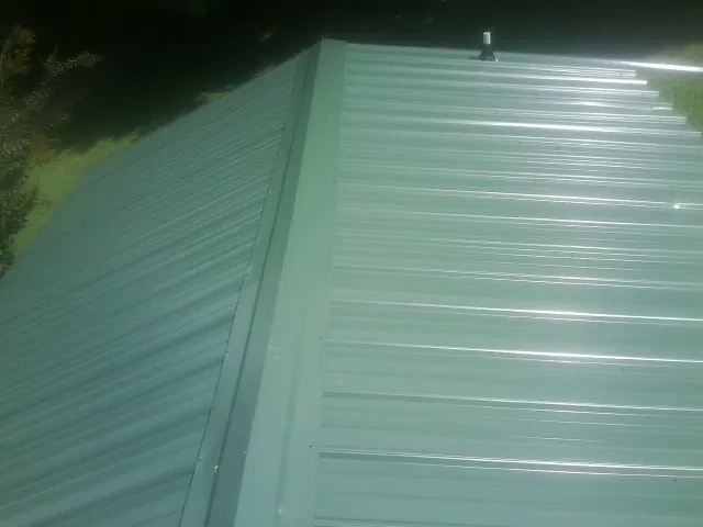New green metal panels meeting at the ridge of a roof — Flat Roof Repair work by our crew in Minoa