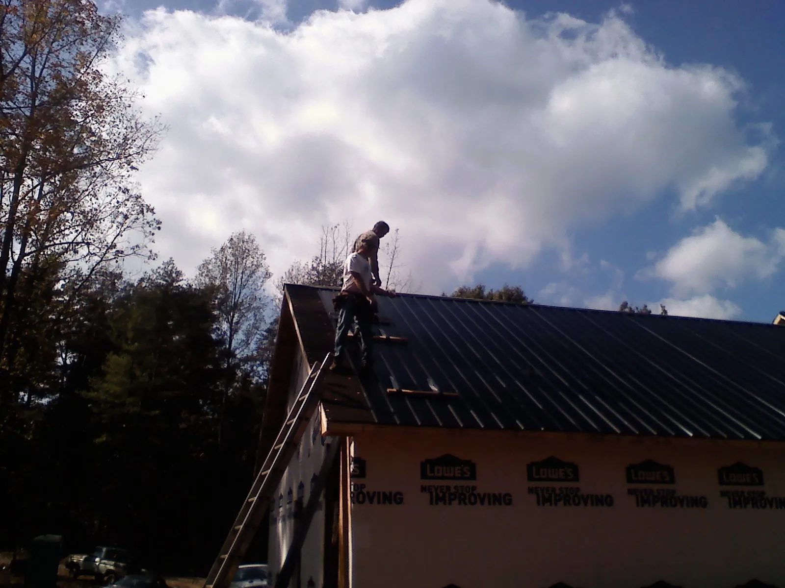 Roofer fastening dark metal panels high against a cloudy sky, from a Roof Inspection job in Minoa