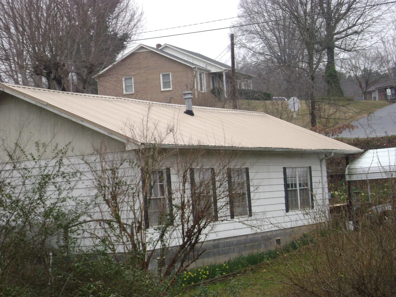 Tan metal roof on a white sided house set into a hillside — Commercial Roofing by Roofing Brothers in Minoa